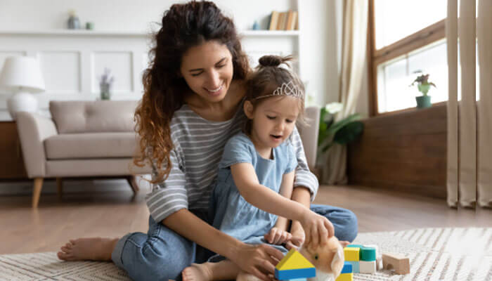 A smiling mother plays with her young daughter on the floor of a cozy living room, symbolizing the nurturing bond and stability emphasized in guides on how to get full custody as a mother.