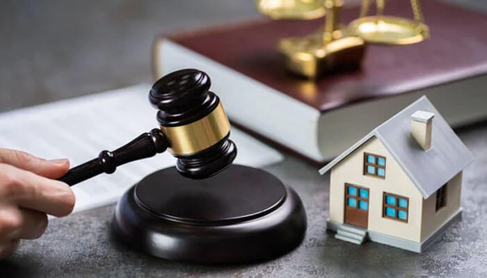 A judge’s gavel beside a miniature house and legal book, representing a family lawsuit involving property or inheritance disputes in court.