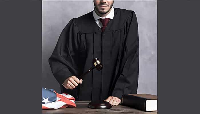 Judge in black robe holding a gavel beside a legal book and American flag, symbolizing justice in a Wrongful Death Claim case.
