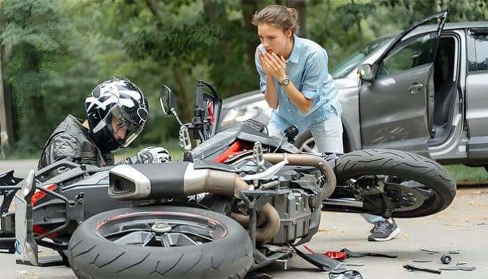 A Brooklyn’s motorcycle accident scene showing a fallen rider beside a crashed motorcycle, with a concerned bystander and a car involved in the collision.