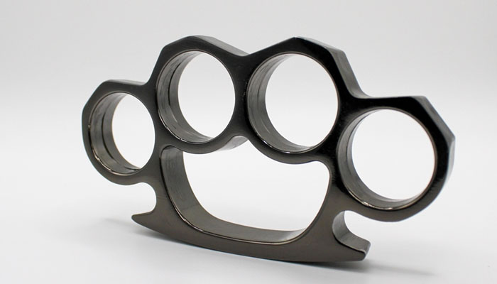 Close-up of a metallic brass knuckle on a white background, used in discussions about self-defense laws and the question: Are brass knuckles legal?
