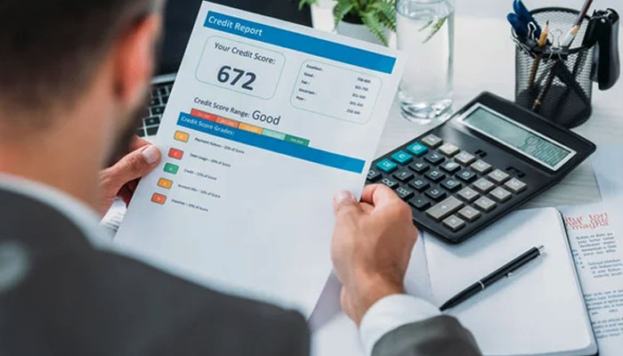 A person reviewing a credit report, with the credit score of 672 highlighted, alongside a calculator, pen, and other paperwork, relevant for rental packet preparation.