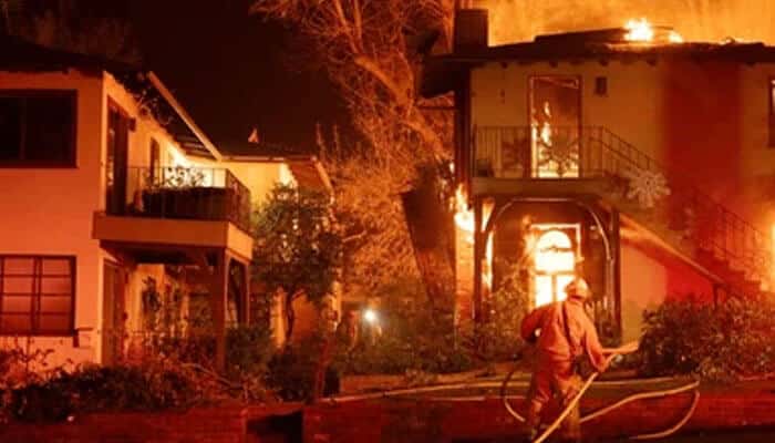Firefighter battles flames engulfing a residential home during a wildfire, representing property damage cases involved in Texas Wildfire Litigation.