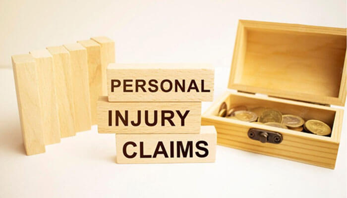 Wooden blocks stacked with the words “Personal Injury Claims” beside an open box of coins, symbolizing compensation and legal claims process.