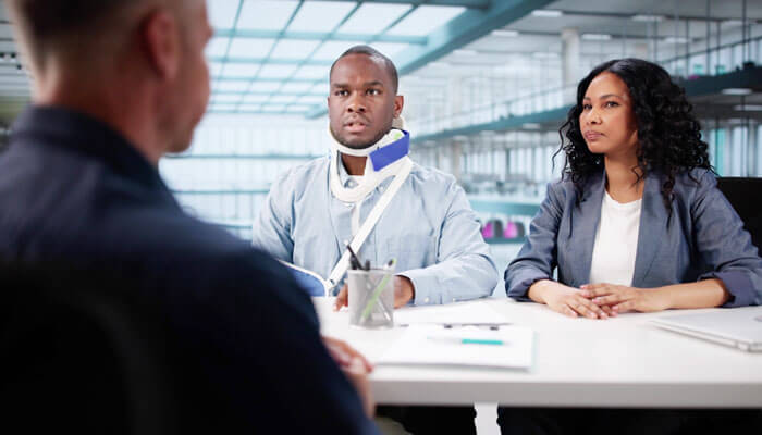 Personal injury attorney consultation with a client wearing a neck brace and their support person, discussing legal matters in an office setting.