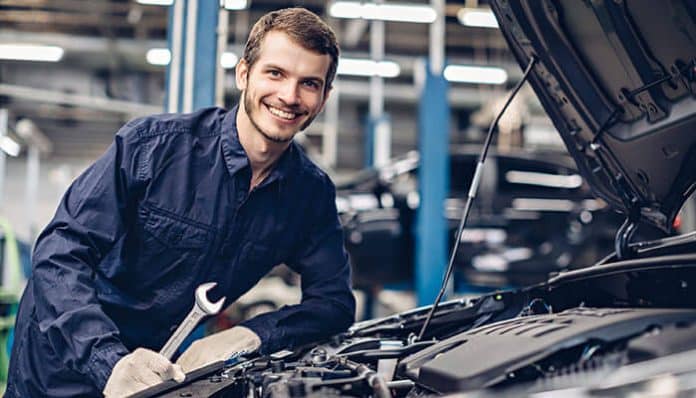 Auto mechanic smiling while working on a car engine in a repair shop, highlighting the importance of documentation and protection against faulty auto parts lawsuits.