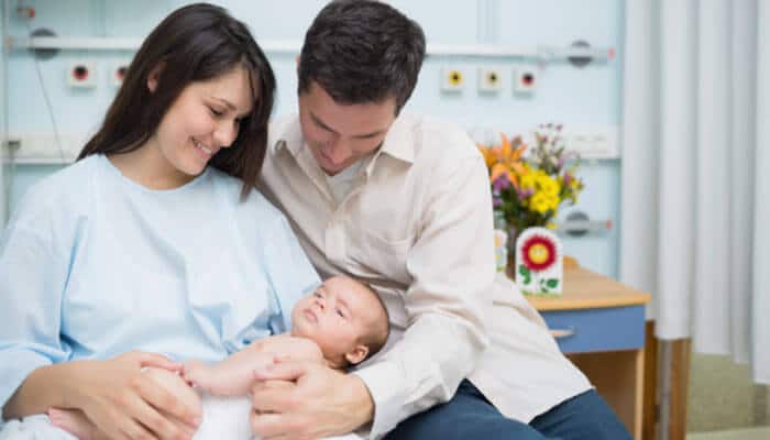 Happy parents holding newborn baby in hospital room | How to Prevent Birth Injuries.