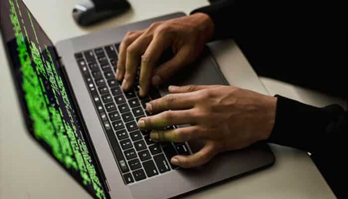 Person typing on a laptop with green code on the screen, representing cybersecurity practices to Know Your Attack Surface and protect digital systems from threats.