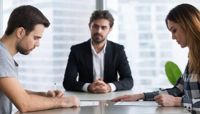 A couple sitting across from each other signing legal documents with a mediator present, illustrating Property Settlement After Divorce.