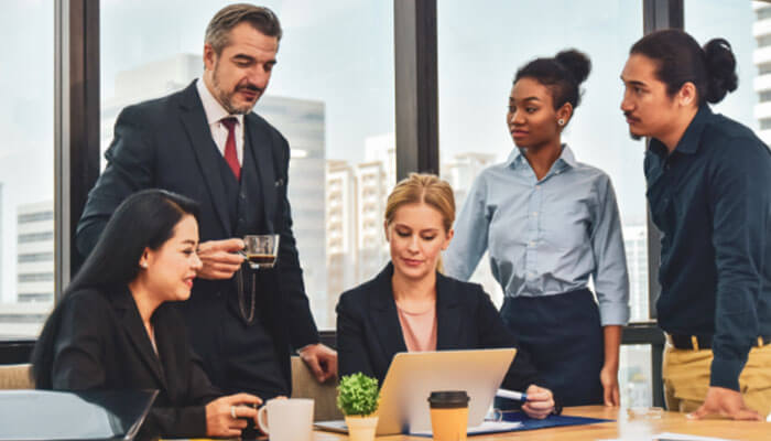 Business Outsourcing team meeting with diverse professionals collaborating around a laptop in a modern office environment.