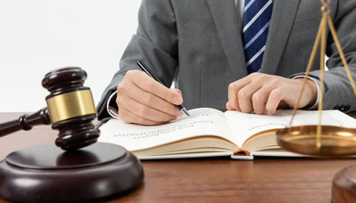 Lawyer in suit writing in a legal book with gavel and scales of justice on desk, symbolizing the decision to hire a lawyer in South Jordan for legal support.