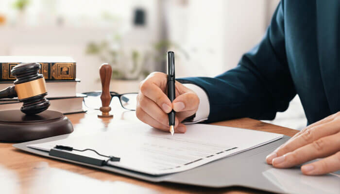 Close-up of a lawyer signing legal documents with gavel and law books on desk, representing the choice to hire a lawyer in South Jordan for legal matters.
