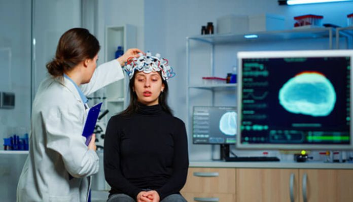 Doctor examining a patient for brain injury symptoms related to CTE with brain scan results on screen.