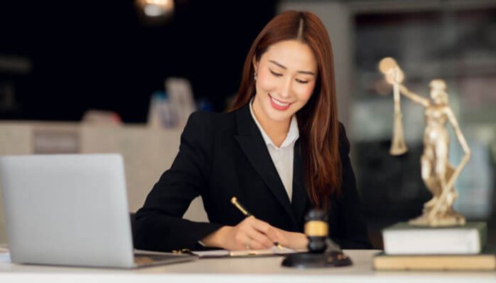 Criminal Defense Lawyer in Dayton writing legal documents at her desk with gavel, laptop, and Lady Justice statue.