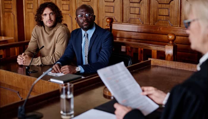 Two men listen to a judge in court, a clear example to understand What is a status hearing in legal proceedings.