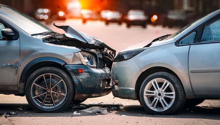 A silver car severely damaged in a car accident with traffic congestion in the background, highlighting the dangers and frequency of car accidents