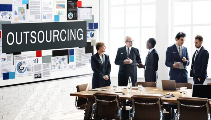 Business Outsourcing meeting with professionals discussing strategies in a modern office, with charts and reports displayed on a large screen.