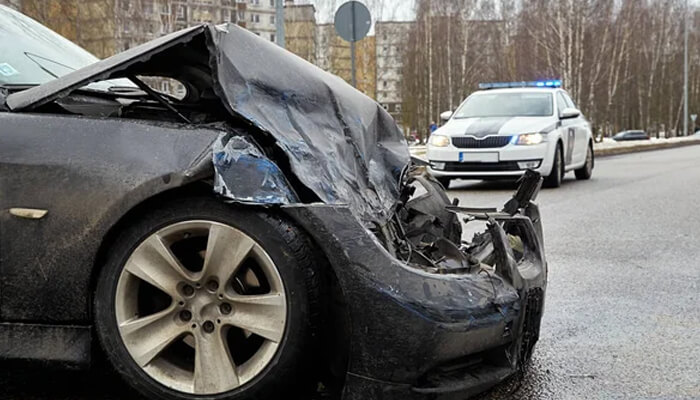 Damaged car after a car crash with police vehicle at the scene, showing accident aftermath and investigation.