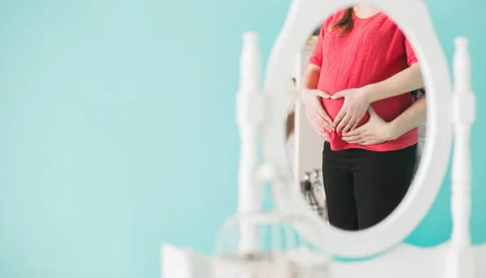 Reflection of a pregnant woman in a mirror forming a heart shape over her belly, symbolizing care and awareness about birth injury and maternal health.