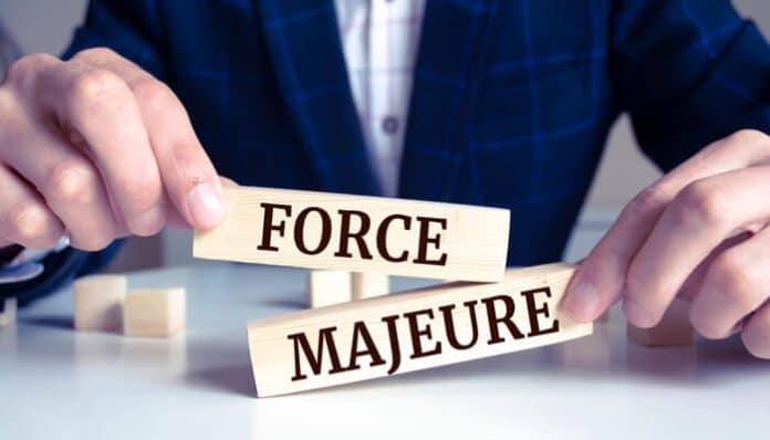 Hands holding wooden blocks labeled Force Majeure, representing legal clauses and unexpected events covered under Force Majeure.
