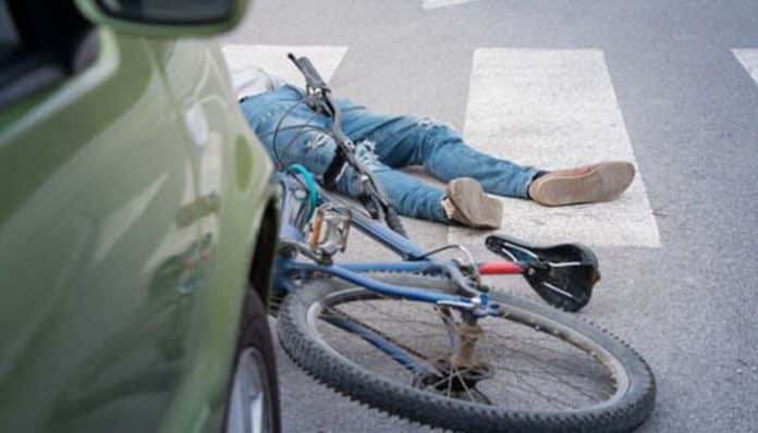 A damaged bicycle lying near a car on a crosswalk after a collision, representing the aftermath of a road crash