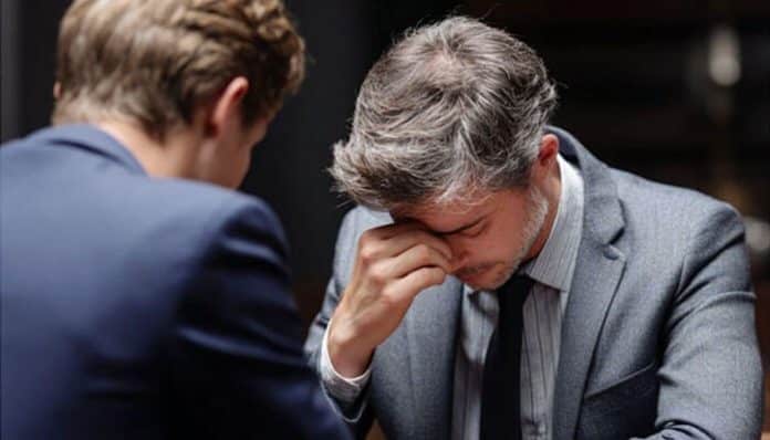 A stressed man in a courtroom setting holding his head in his hand while speaking with a lawyer, symbolizing the emotional toll of Criminal Proceedings.