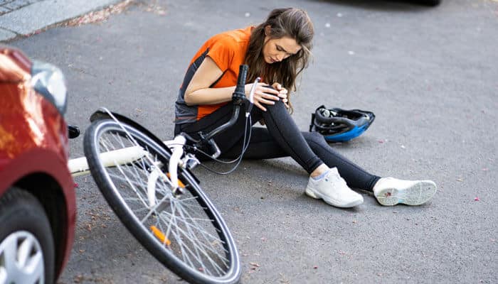 A woman sitting injured on the road beside a fallen bicycle after a collision with a car, symbolizing the aftermath of a crash and the need for a Bicycle Accident Settlement in Austin.