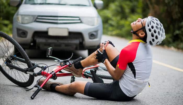 What You Need to Cyclist injured on the road after collision with a car, holding leg in pain — illustrating the need for a Bicycle Injury Claim.