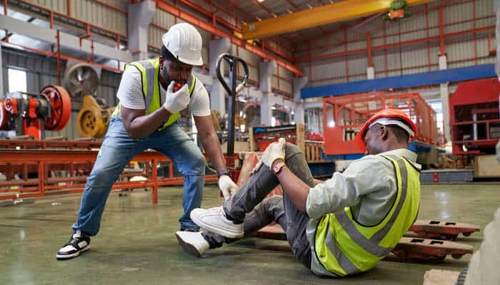 Who Can Be Held Responsible for Negligent Security - Myleagalopinion - My Legal Opinion An injured construction worker sitting on the factory floor holding his leg while a coworker calls for help — illustrating workplace injury caused by negligent security and unsafe premises.