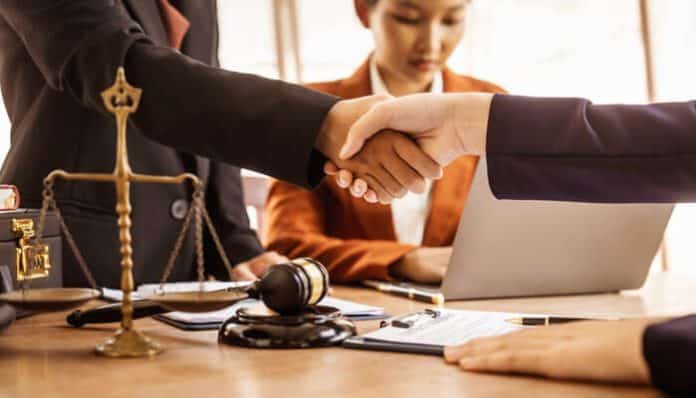 Law firm attorneys shaking hands at a desk with legal documents, gavel, and scales of justice, symbolizing trusted legal representation.