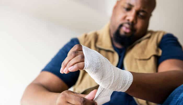 A man carefully wrapping a bandage around his injured hand, illustrating the type of injury that might lead to filing a Personal Injury Claim.