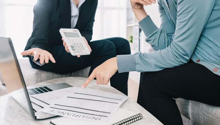 Two professionals reviewing insurance documents with a calculator and laptop, discussing how compensation is calculated in personal injury cases.