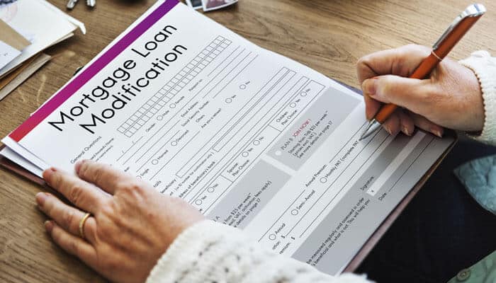 A person filling out a Mortgage Loan Modification form, illustrating the process of applying for a modification to adjust mortgage terms for financial relief.