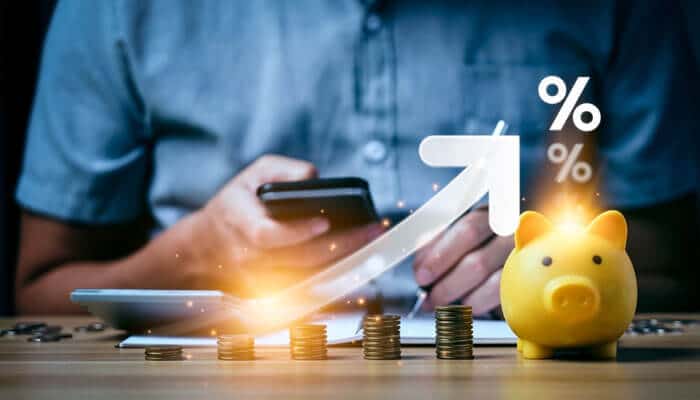 A person using a smartphone beside stacked coins and a piggy bank with a rising arrow symbolizing growth — representing Smart Business Leaders on Personal Saving Habits and financial success.