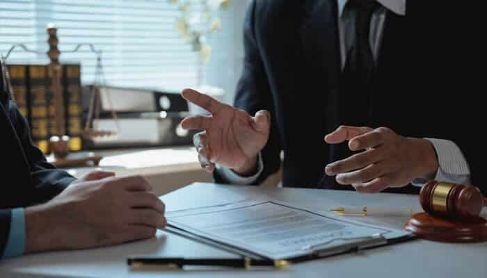 A lawyer consulting with a client about legal options after a criminal arrest, showing a discussion with legal documents, a gavel, and books in a law office.