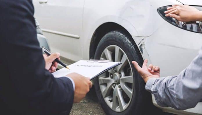 Insurance adjuster inspecting car damage and taking notes for a Car Accident Claim after a collision.