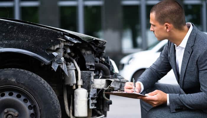 Insurance adjuster inspecting a damaged car to assess Car Accident Compensation after a collision.