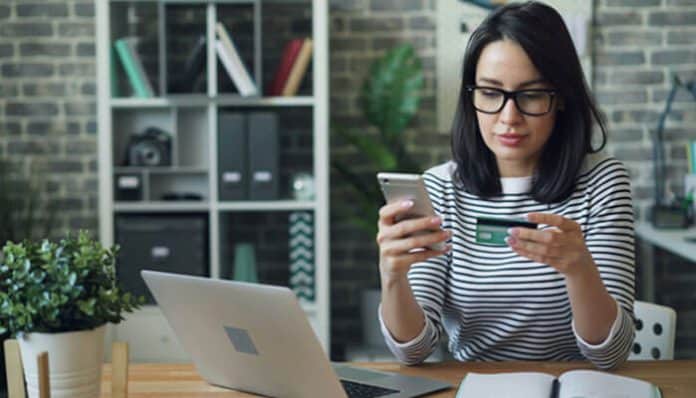 A woman using her phone and credit card, highlighting the importance of understanding when and why banks may freeze accounts and how consumers can address the situation.
