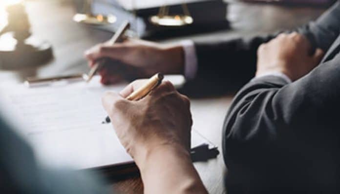 Close-up of two individuals signing legal documents, highlighting the importance of careful attention while drafting an affidavit.