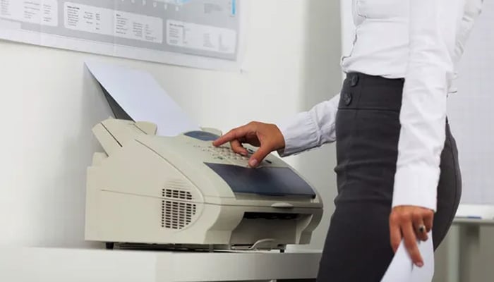 Cost-Effective Solutions for Document Management and Transmission - Mylegalopinion - My Legal Opinion Using an outdated fax machine: A woman operates a traditional fax machine, highlighting the need for modern solutions like an online faxing program for efficient communication.