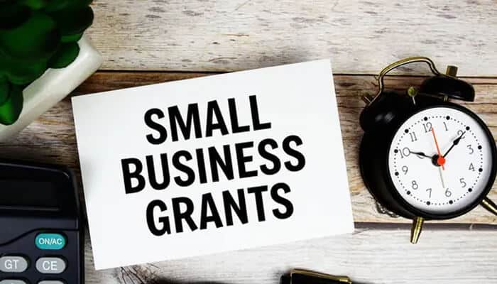Grants for small businesses - Myleagalopinion - My Legal Opinion A desk with a card displaying the words Small Business Grants beside a clock, representing funding opportunities for small business owners.