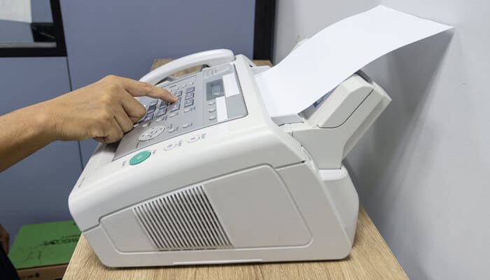 How Online Faxing Programs Have Transformed the Way Businesses Communicate - Myleagalopinion - My Legal Opinion Person using a traditional fax machine, representing the older method of faxing compared to the efficiency of Online Faxing Programs.