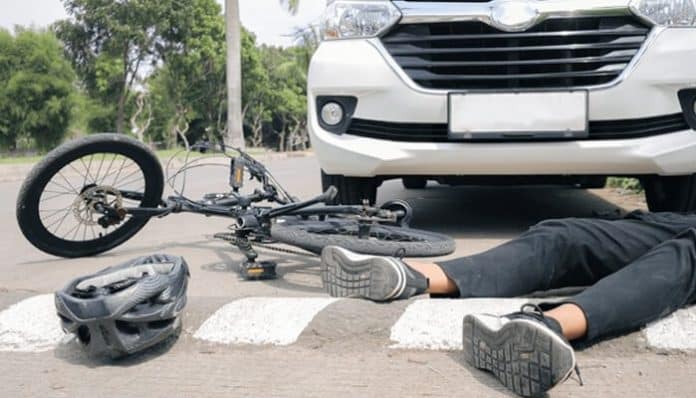 A bicycle accident scene showing a person lying on the road near a white car with their bicycle beside them, symbolizing the need for a bicycle lawyer.
