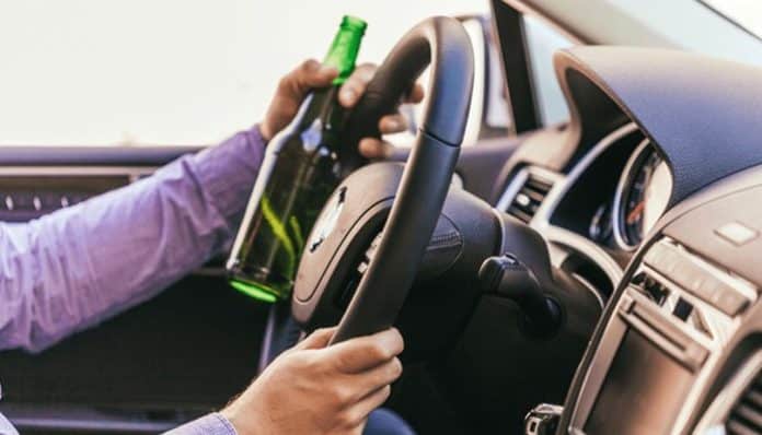 Person holding a bottle of alcohol while driving, symbolizing the dangers of drunk driving in car accident cases.