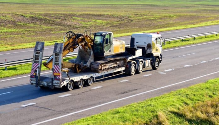 A large truck transporting heavy construction equipment on a flatbed trailer, illustrating usage details relevant to a trailer rental agreement.