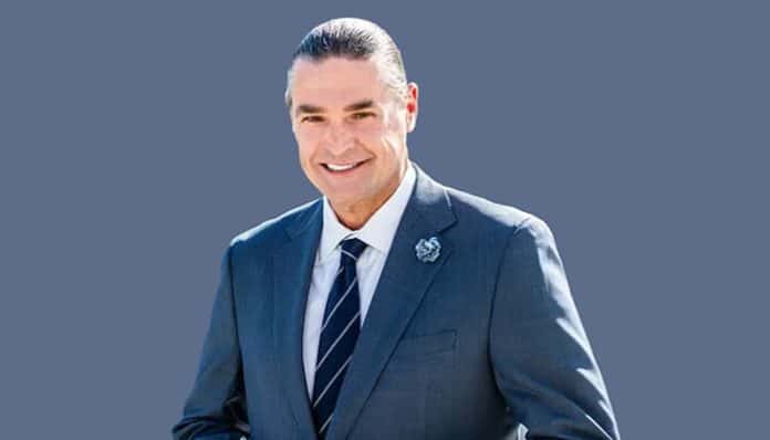Jeffrey Phillips smiling in a suit, with a background of a solid color, looking professional and confident.