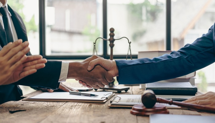 Litigation and Negotiation - Myleagalopinion - My Legal Opinion Two business professionals shaking hands over legal documents, symbolizing Class Action Lawsuits and legal agreements.