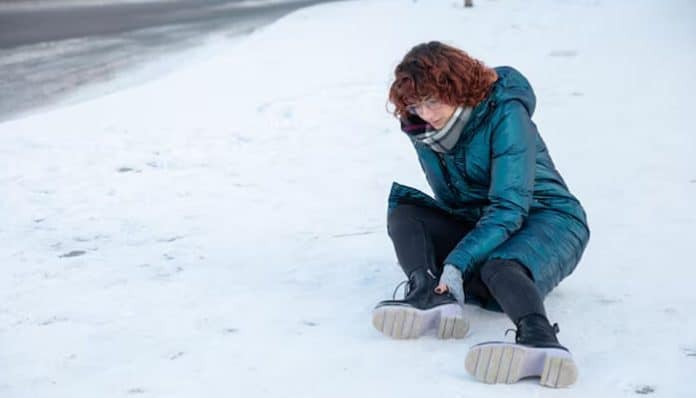 Person injured after slipping on winter pavement, showing how invisible ice causes serious injuries to legs, hips, and lower body.