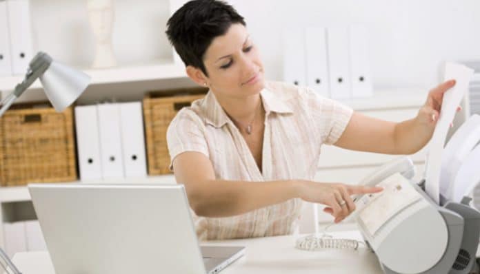 Using an online faxing program: A woman in an office setting operating a fax machine, illustrating the convenience of modern digital fax solutions for businesses