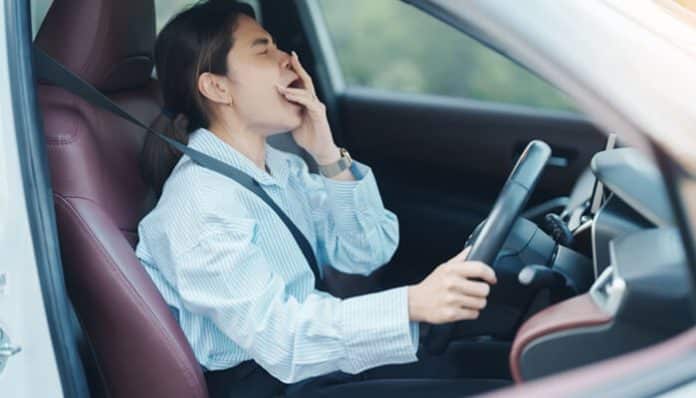 Young driver yawning behind the wheel, showing fatigue and risk of a drowsy car driving accident on the road.